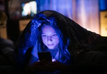 Little girl in bed under a blanket looking at the smartphone at night.