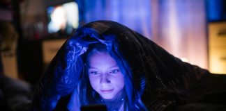 Little girl in bed under a blanket looking at the smartphone at night.